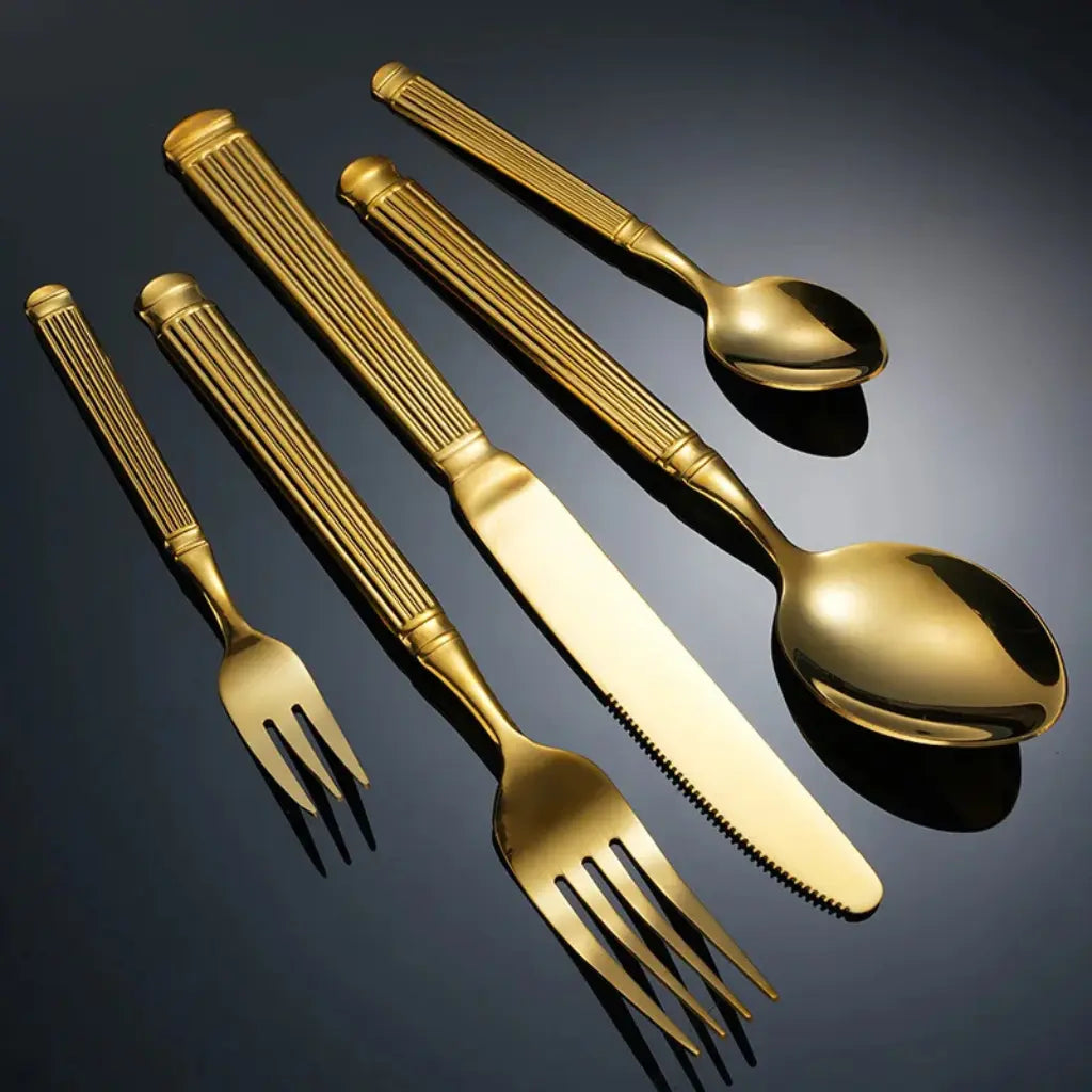Composição horizontal do faqueiro dourado Grand Élysée com talheres espalhados sobre fundo azul escuro.