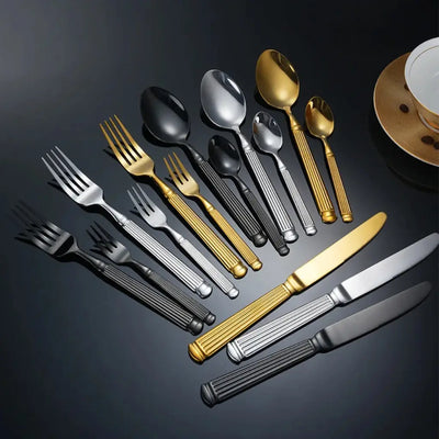 Faqueiro Grand Élysée com talheres prata, dourado e preto em composição elegante sobre fundo escuro sofisticado.