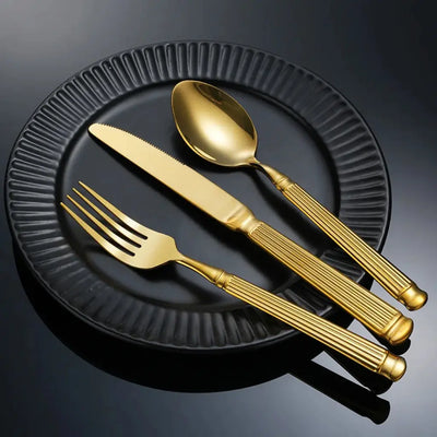 Faqueiro dourado Grand Élysée em prato preto fosco, formando uma composição moderna e luxuosa.