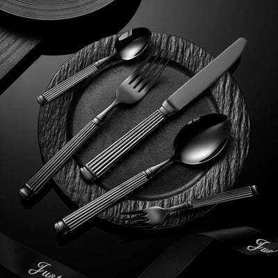 Faqueiro Grand Élysée preto em aço inox sobre prato preto texturizado. Composição elegante para mesa posta sofisticada.