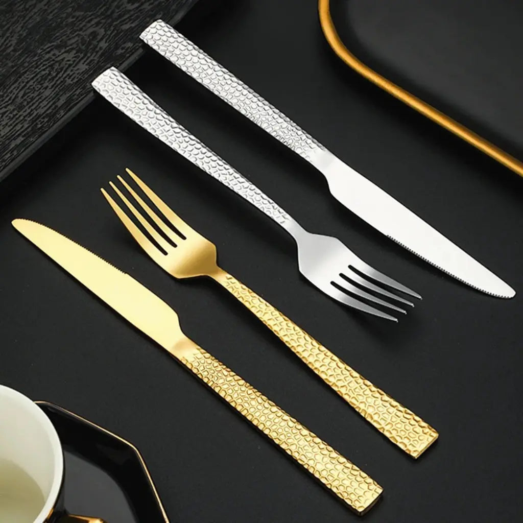 Talheres de luxo dourados e prateados sobre bandeja preta – contraste elegante que valoriza a experiência à mesa.