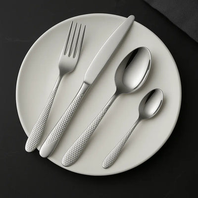Faqueiro inox 24 peças com cabo texturizado, dispostos sobre prato branco em mesa escura sofisticada