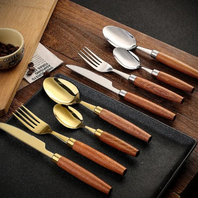 Conjunto dourado com cabo de madeira exibido sobre mesa preta com pratos e guardanapos, ideal para jantares especiais.